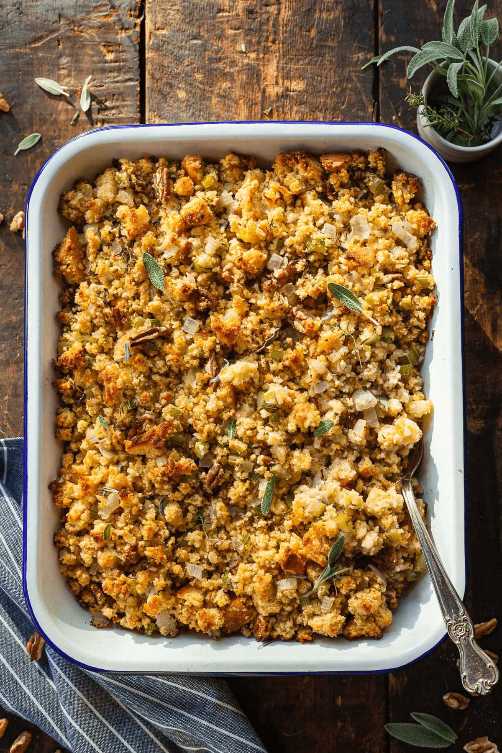 Cubes of golden cornbread mixed with pecans, celery, and herbs in a casserole dish with a crumbly texture.