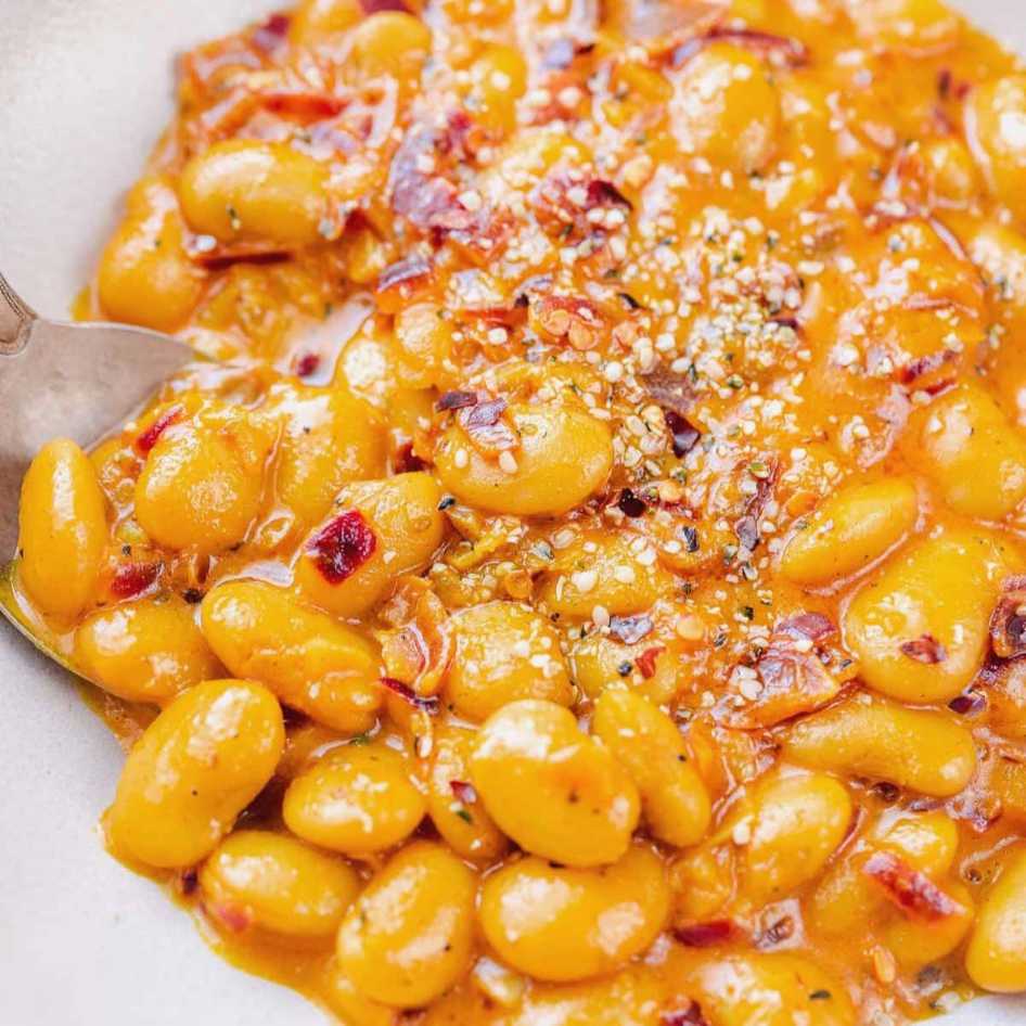 Large white beans in a creamy tomato sauce with diced tomatoes and fresh basil in a shallow dish.