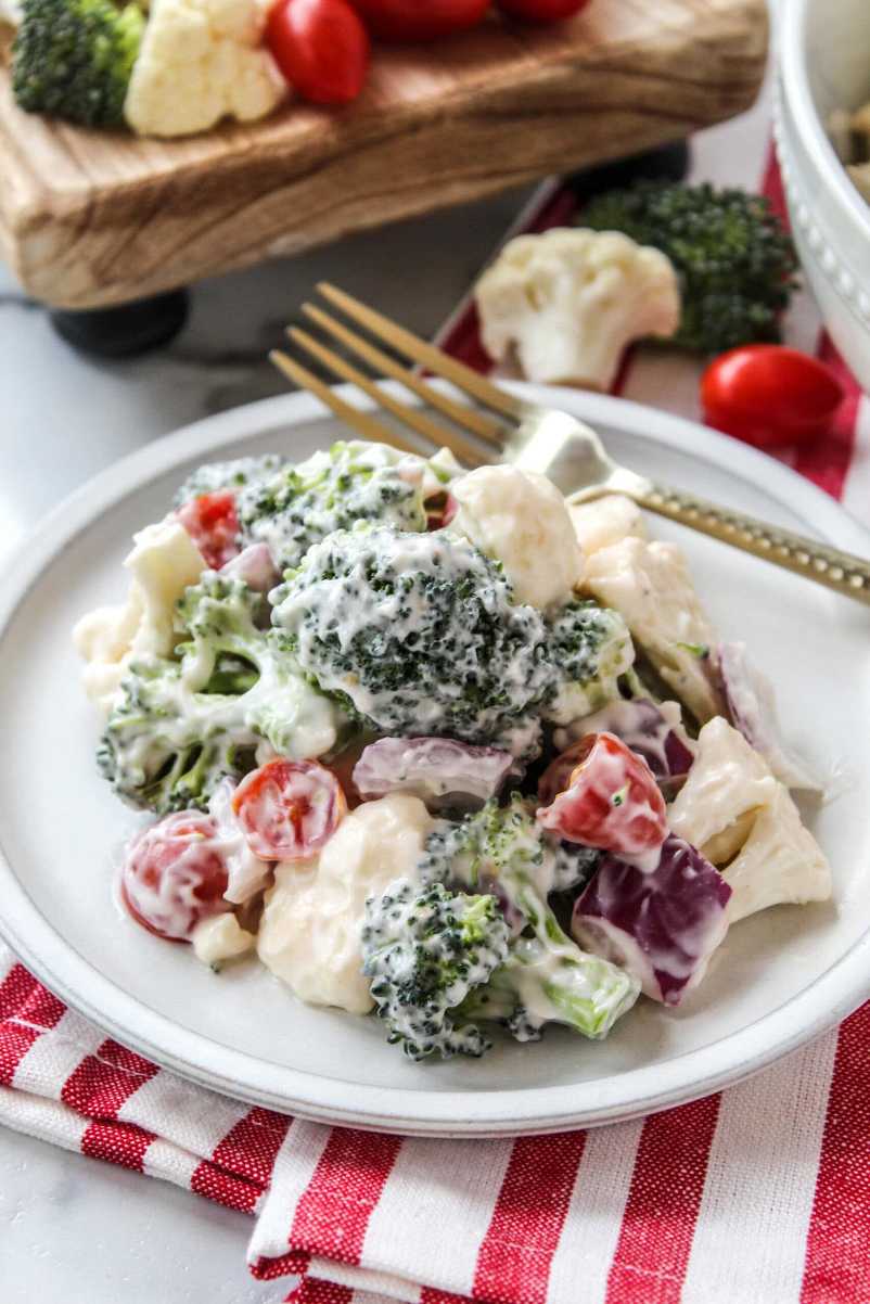 Chopped broccoli and cauliflower florets tossed in a creamy dressing with dried cranberries and almonds in a bowl.