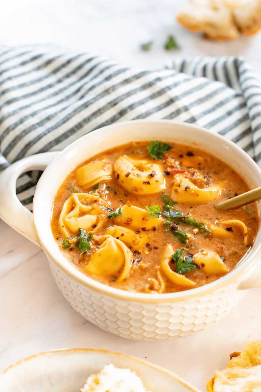 Heaping bowl of creamy tomato soup with cheese tortellini, garnished with basil and parmesan.